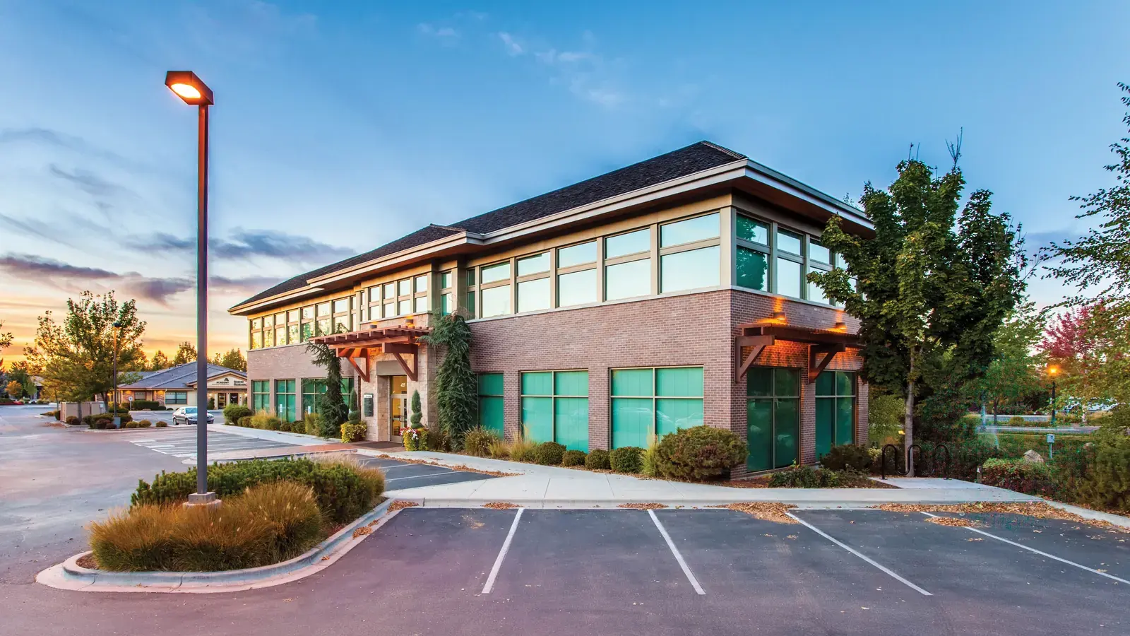 Two-story brick office building with a parking lot at dusk